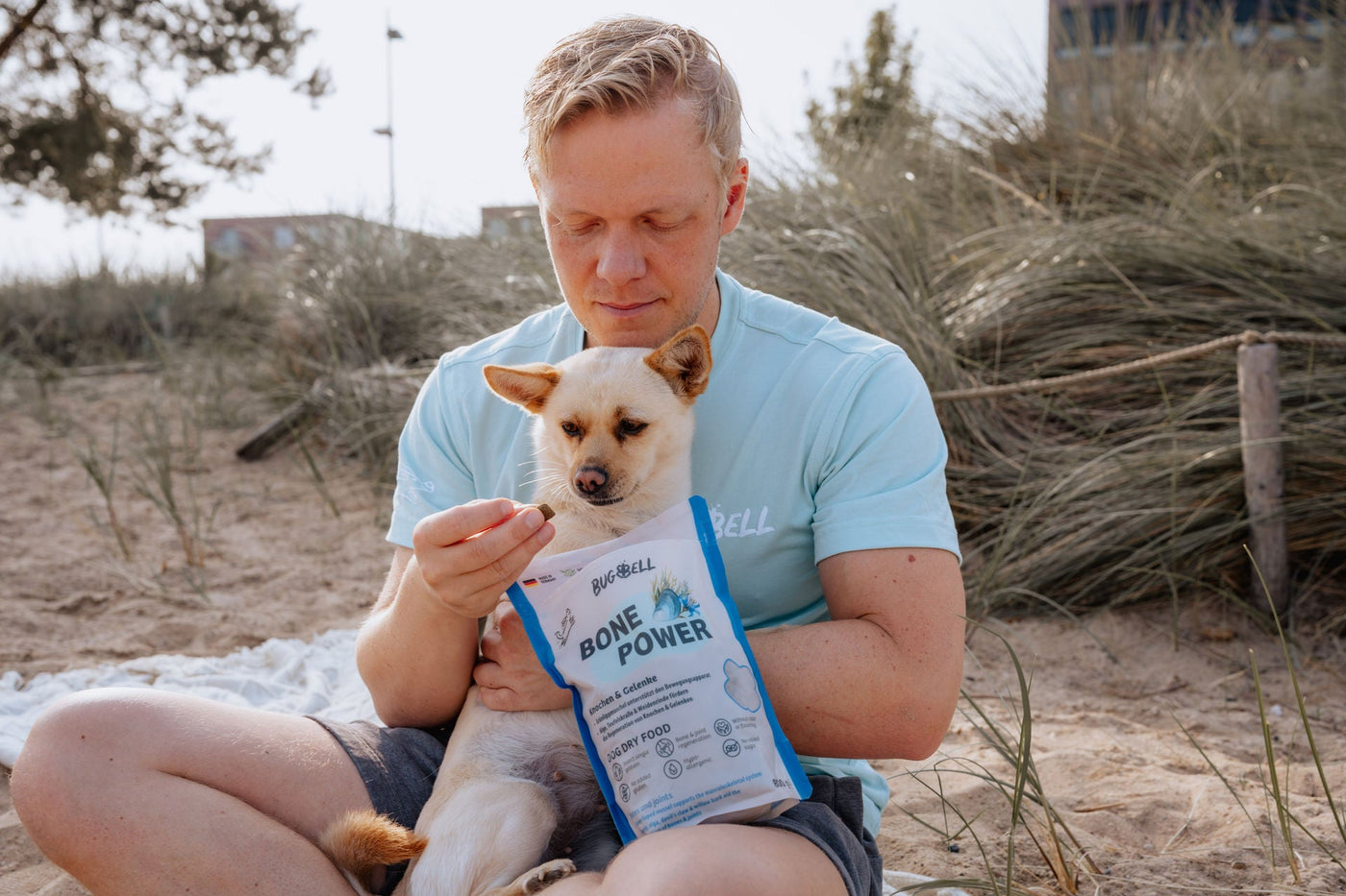 Mann und Hund haben das Trockenfutter für Gelenkunterstützung in der Hand am Strand
